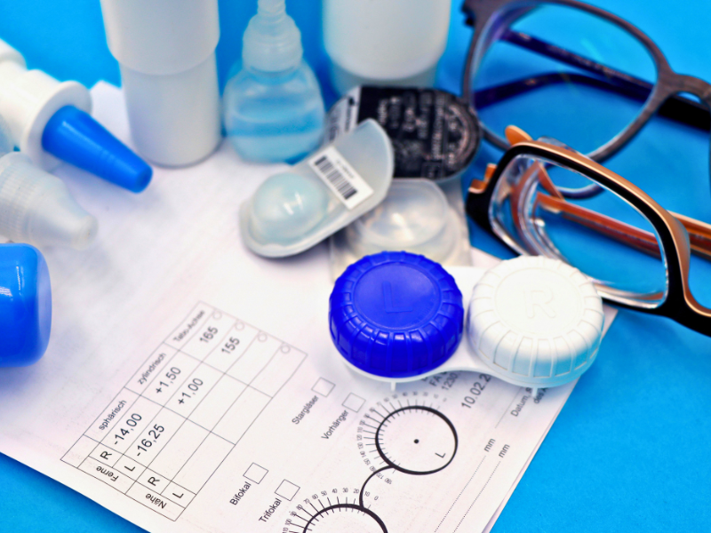 Eyeglasses prescription form, contact lens case, eyeglasses, and eye care products on a bright blue background 