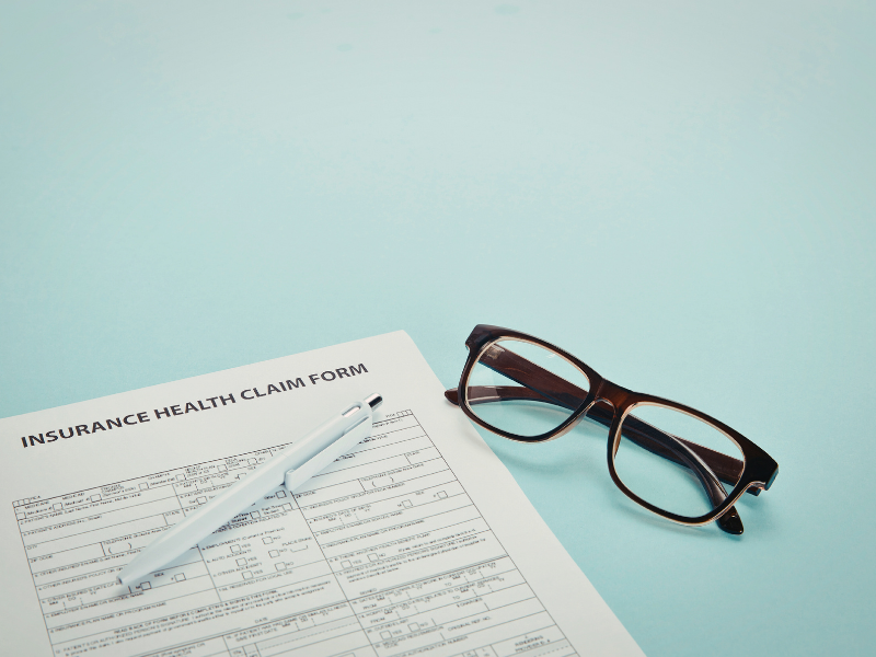 Brown eyeglasses resting on an insurance health claim form with a white pen 