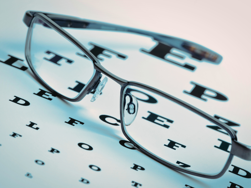 Black-rimmed eyeglasses placed on an eye chart with large letters 